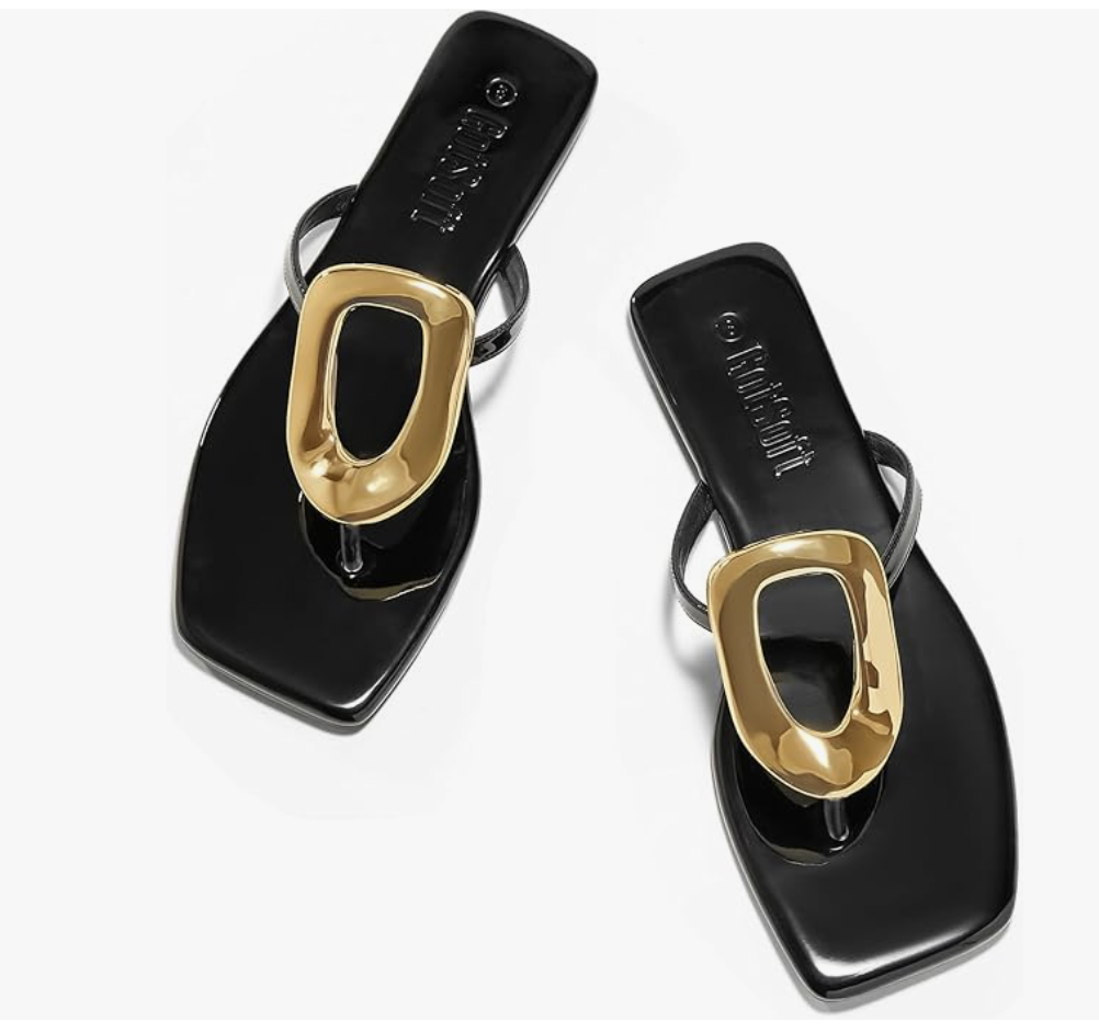 A pair of minimalist black leather-look thong sandals with a modern square toe and a chunky gold oval ring detail on the strap, styled for a resort vacation.