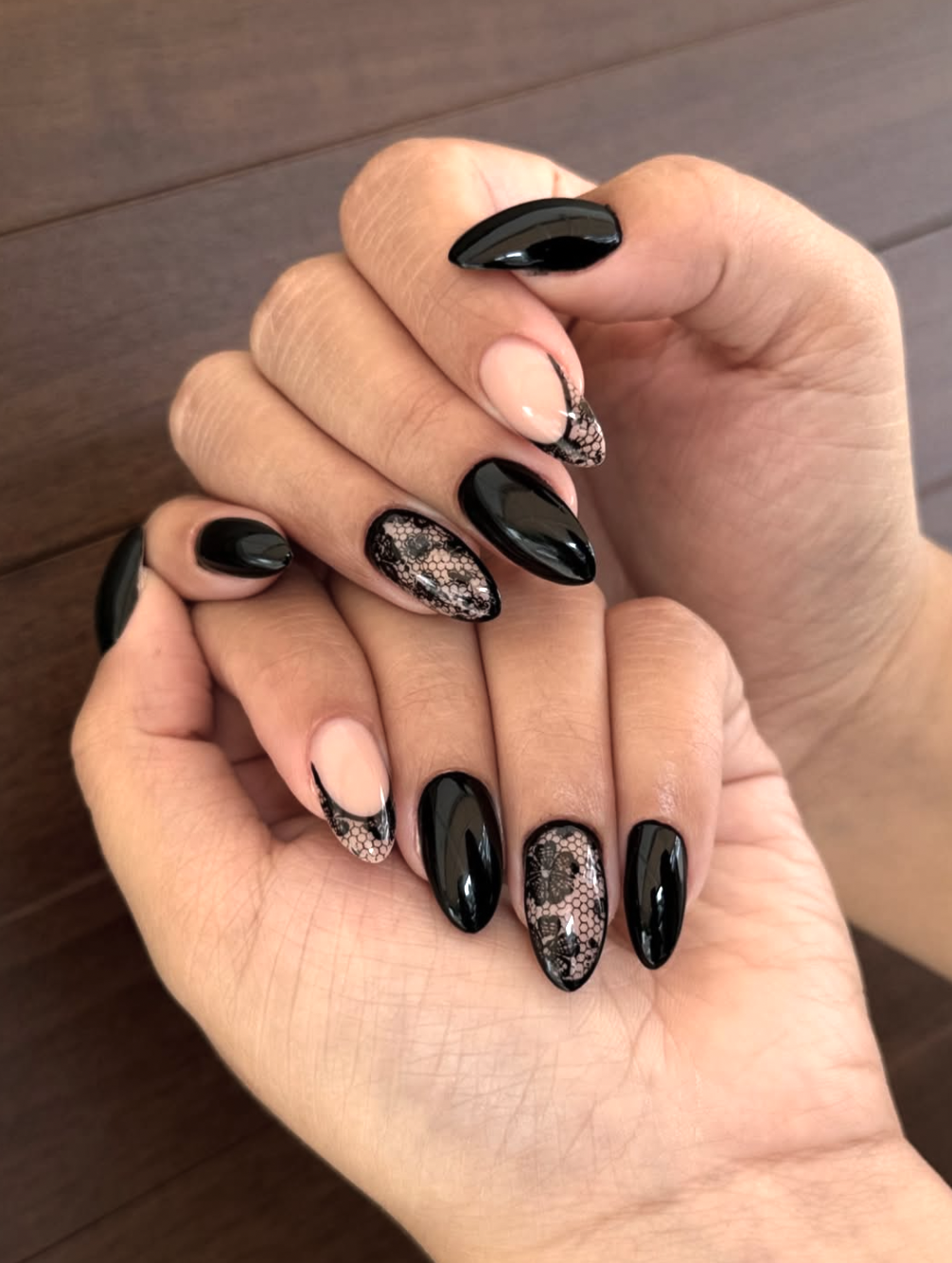 Long almond-shaped nails with a mix of solid black polish, a black lace French tip design, and one full-coverage black lace accent nail on a nude base.