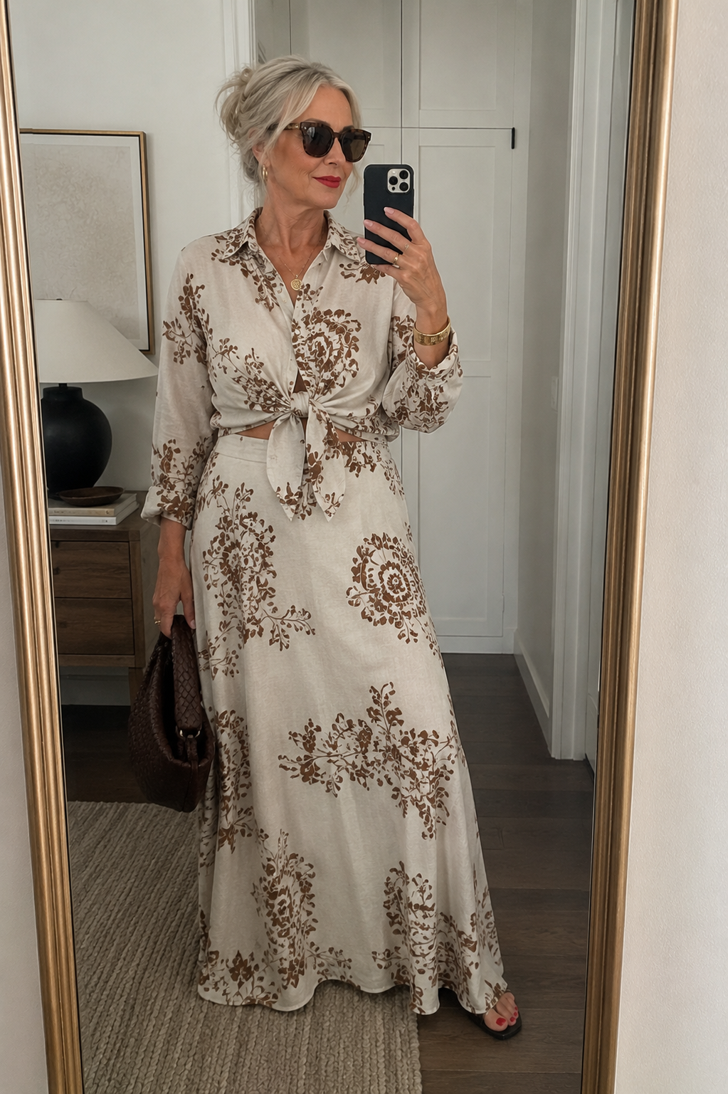 Close-up of a woman in a mirror selfie wearing a matching linen maxi skirt and tie-front long-sleeve top set in a brown floral paisley print.