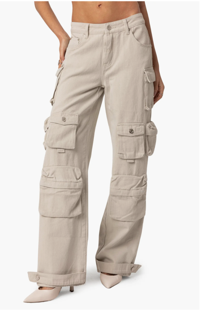 A close-up of a person wearing beige high-waisted cargo pants featuring multiple stacked utility pockets on the legs and a wide-leg silhouette.