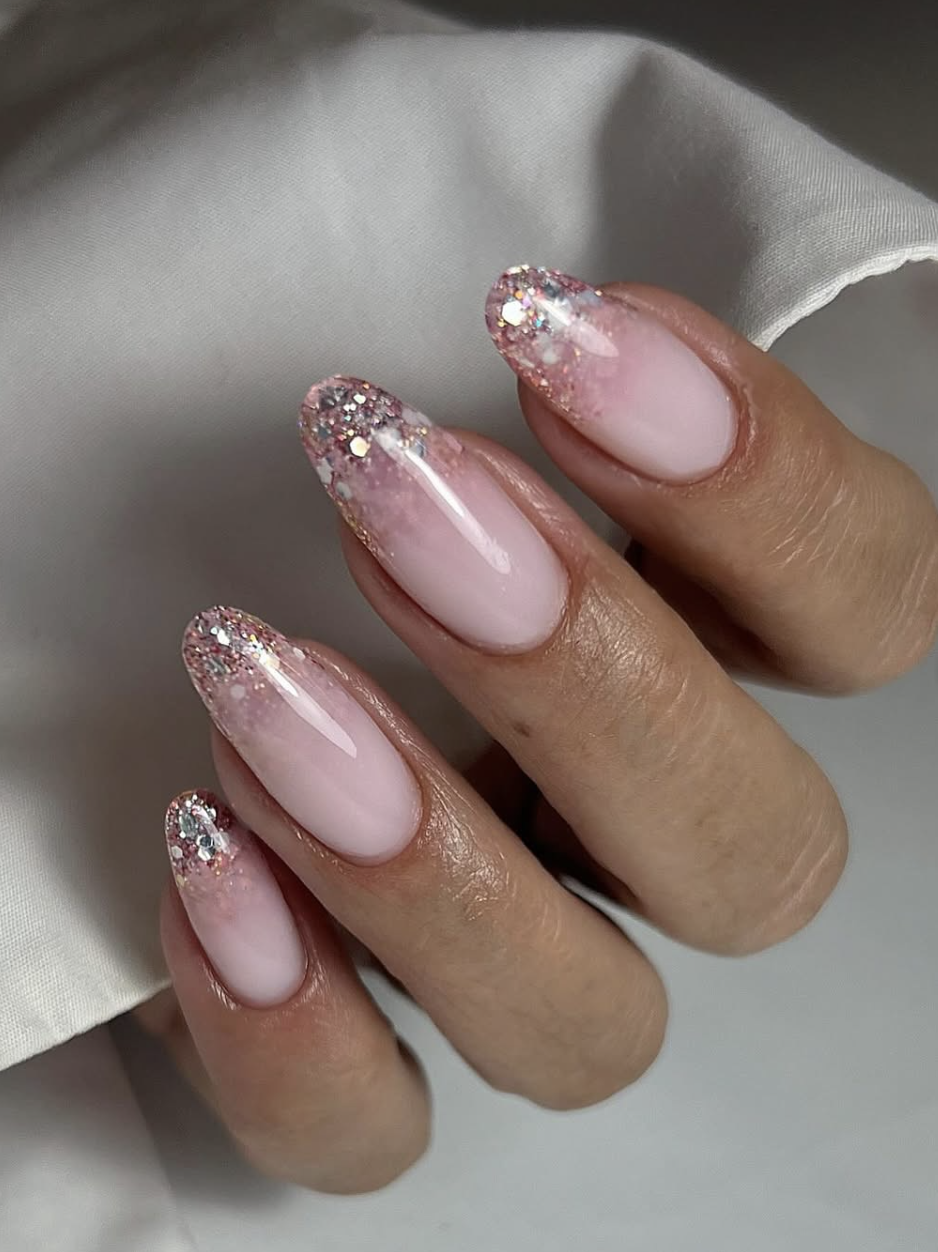Long, oval-shaped nails with a glossy, semi-sheer pink base fading into a dreamy, reflective silver glitter gradient at the tips.