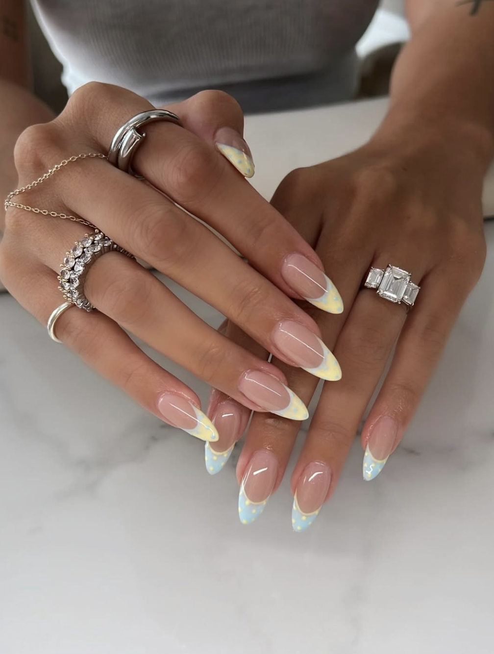 Long almond shaped nails with a natural base and double-layered pastel yellow and white French tips.