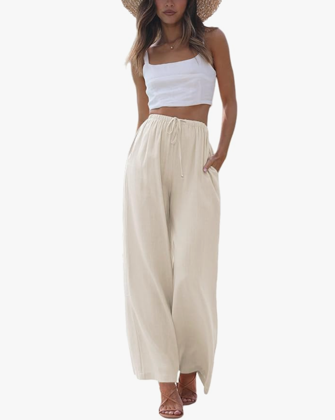 A woman wearing beige high-waisted cotton-linen palazzo pants with a wide-leg silhouette and a drawstring waist, styled with a white cropped tank top for a breezy summer beach look.