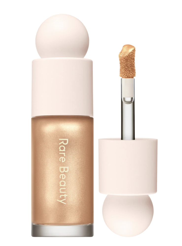Rare Beauty Positive Light Liquid Luminizer bottle with wand applicator showing champagne gold liquid highlighter pigments against a transparent background.