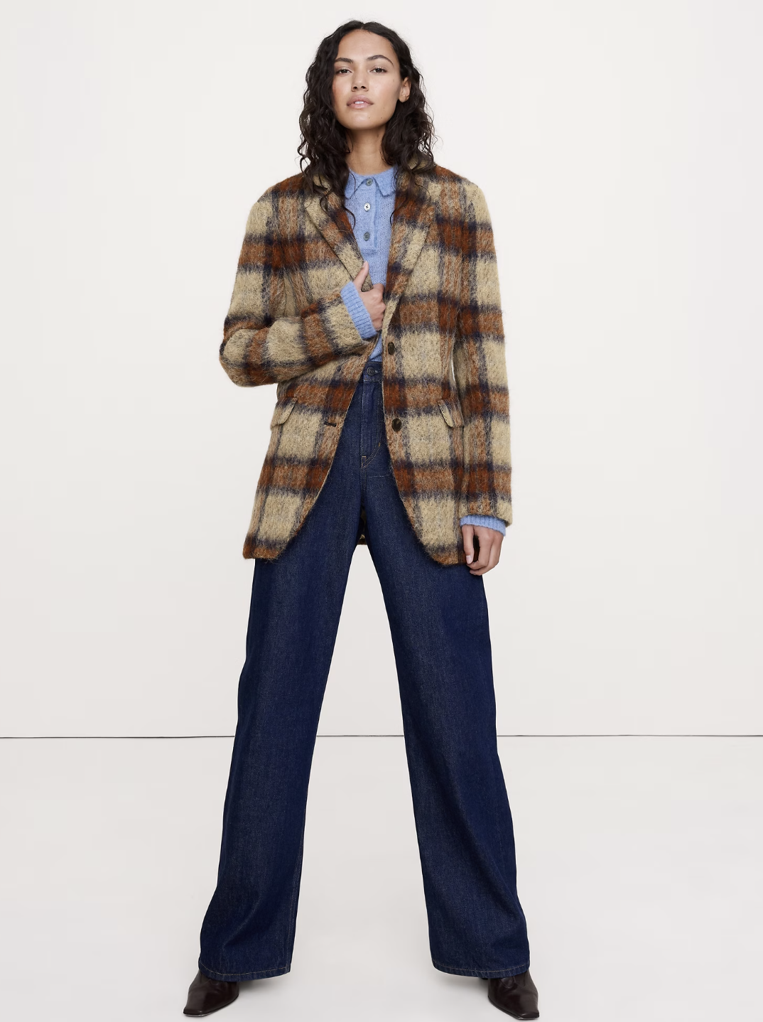 A woman wearing a dark brown structured blazer, a black beret, and a tie, leaning against a stone pillar to showcase the poetcore aesthetic.