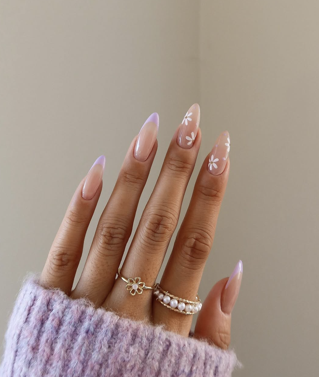 Long oval-shaped nude nails featuring tiny, minimalist white micro-flowers scattered across a sheer base.