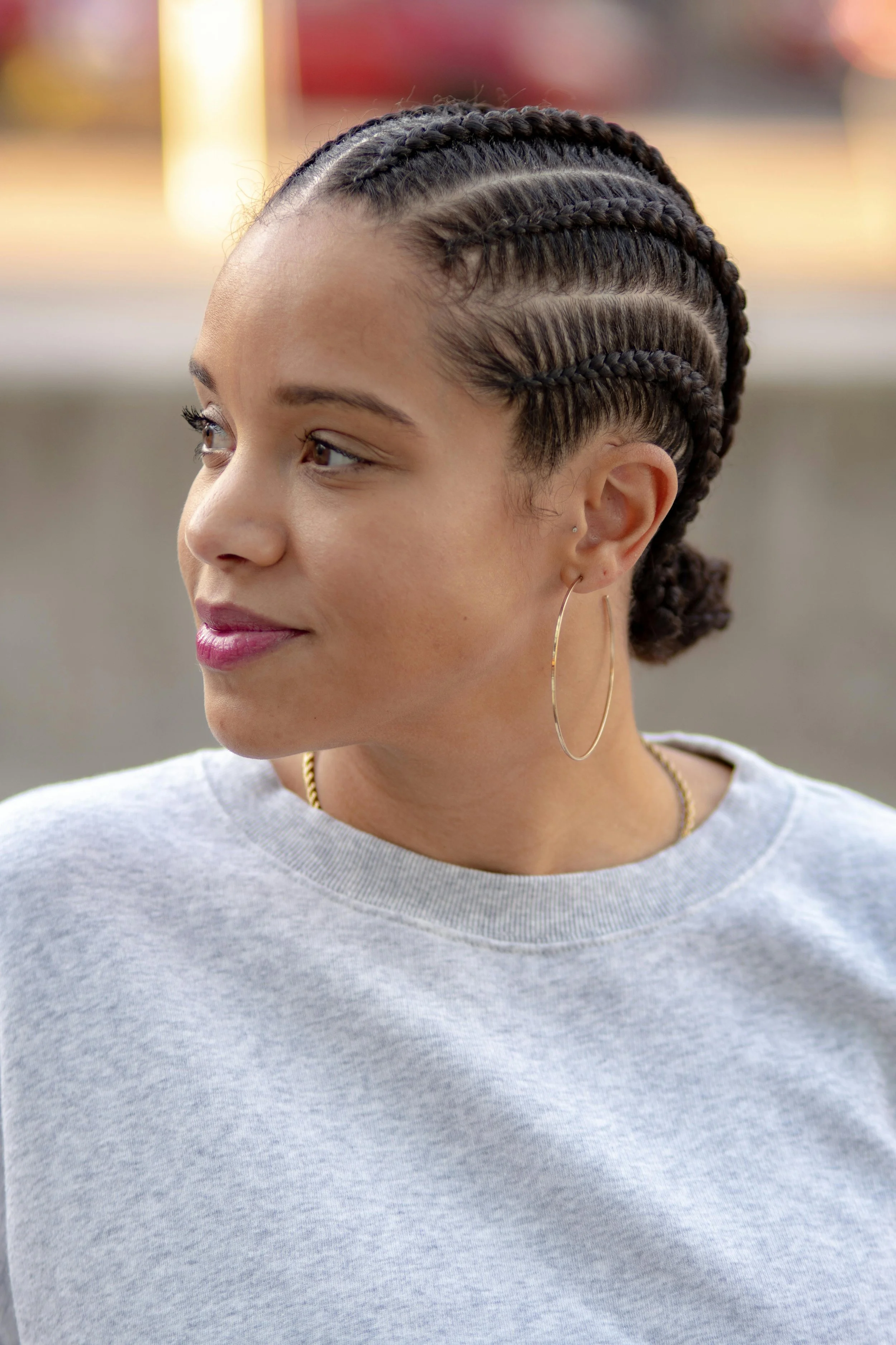 A woman with a sleek bun wearing gold hoop earrings and a gray sweatshirt, representing a clean wash day aesthetic for a guide on the best scalp massagers and scrubbers for natural hair.