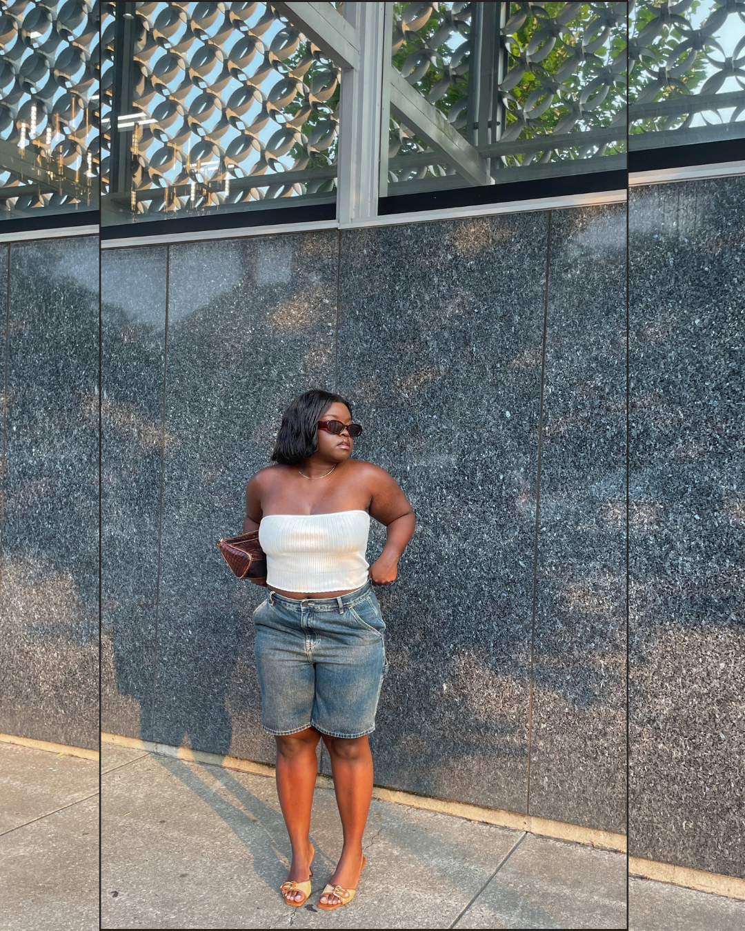 A woman wearing a white strapless tube top and mid-wash denim Bermuda shorts with a raw hem, styled with orange sandals and a brown clutch.