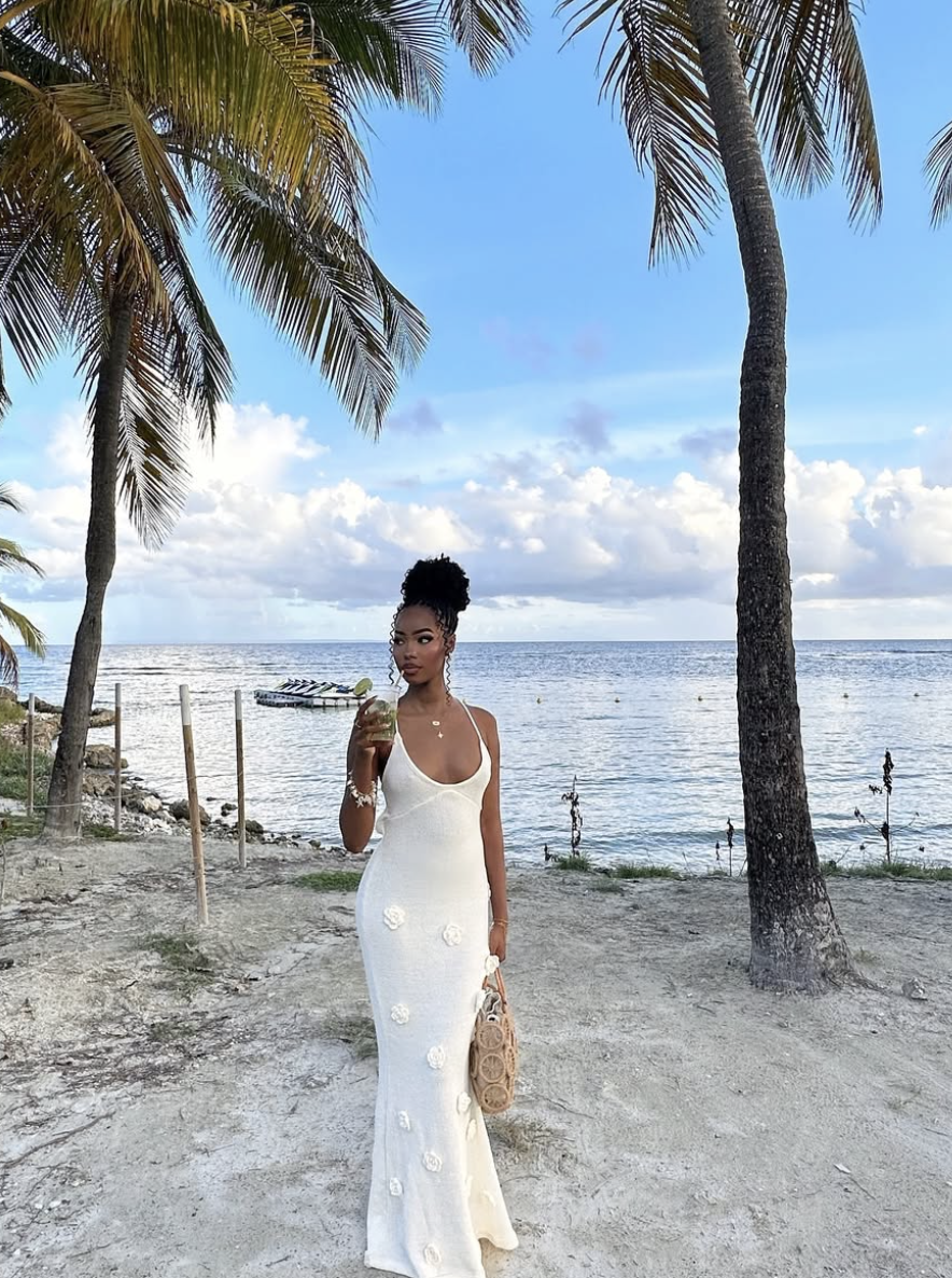 A woman wearing a flowy white maxi dress paired with thin, strappy neutral-toned sandals.