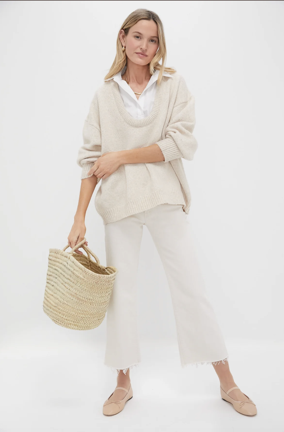 Model wearing a cream short-sleeve crewneck sweater with wide-leg trousers, a woven shoulder bag, and pink ballet flats on a white background.