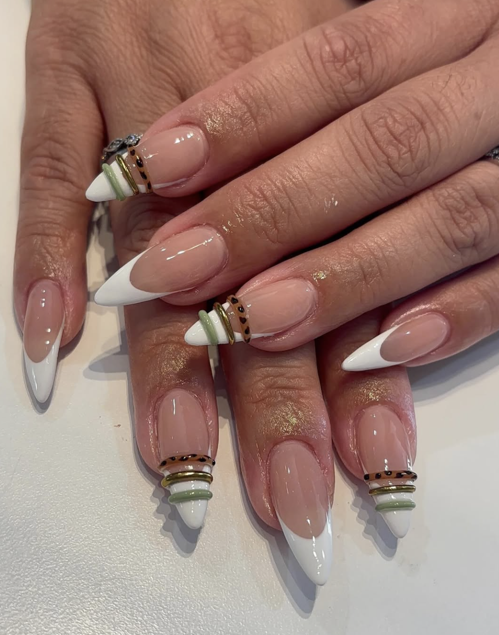 Almond French tip nails with a nude base and three thin 3D bands in olive, brown, and gold wrapped around the center.