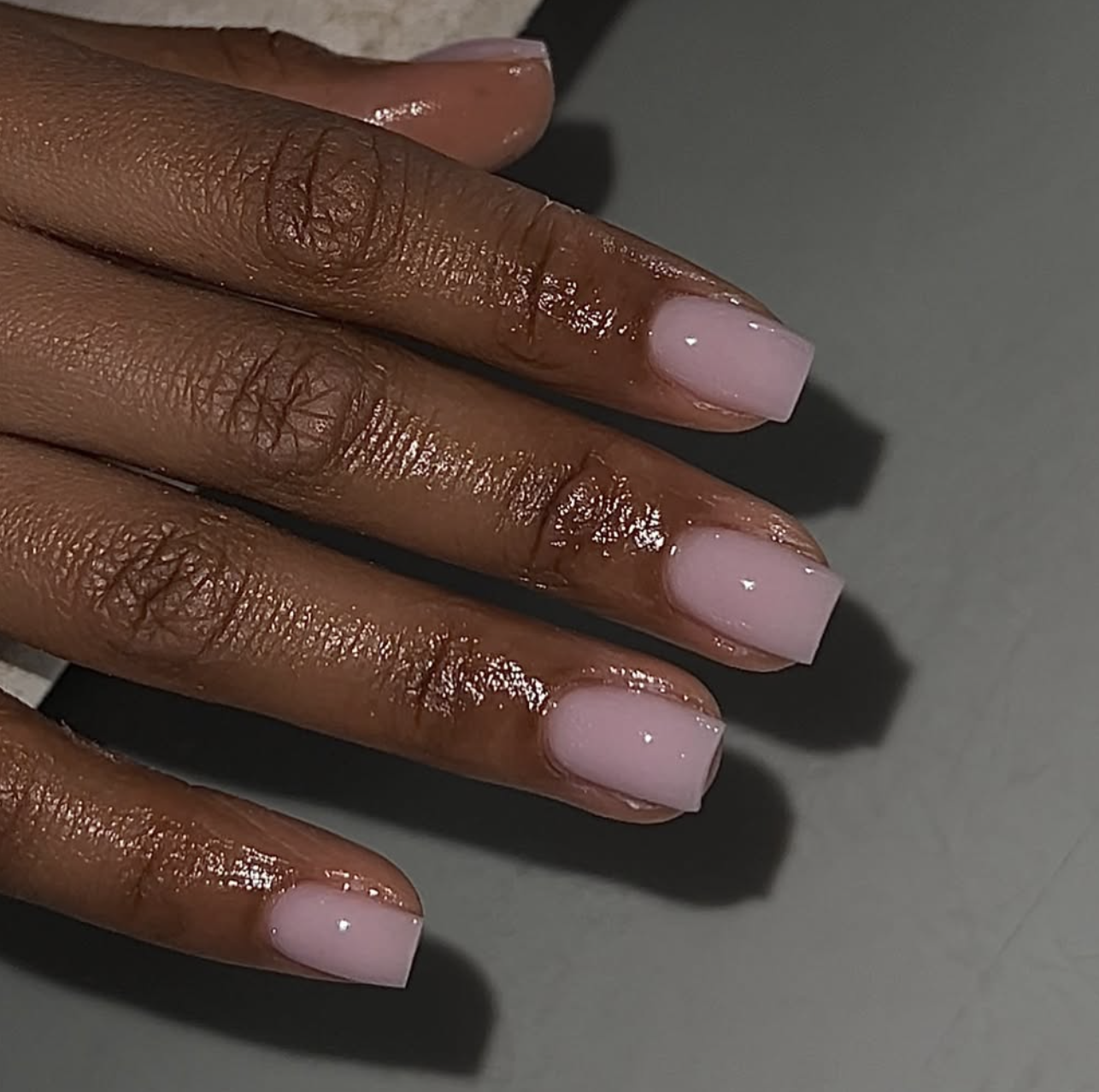 lose-up of a hand with soft pink nails in a squared shape with a high-shine, glossy finish.