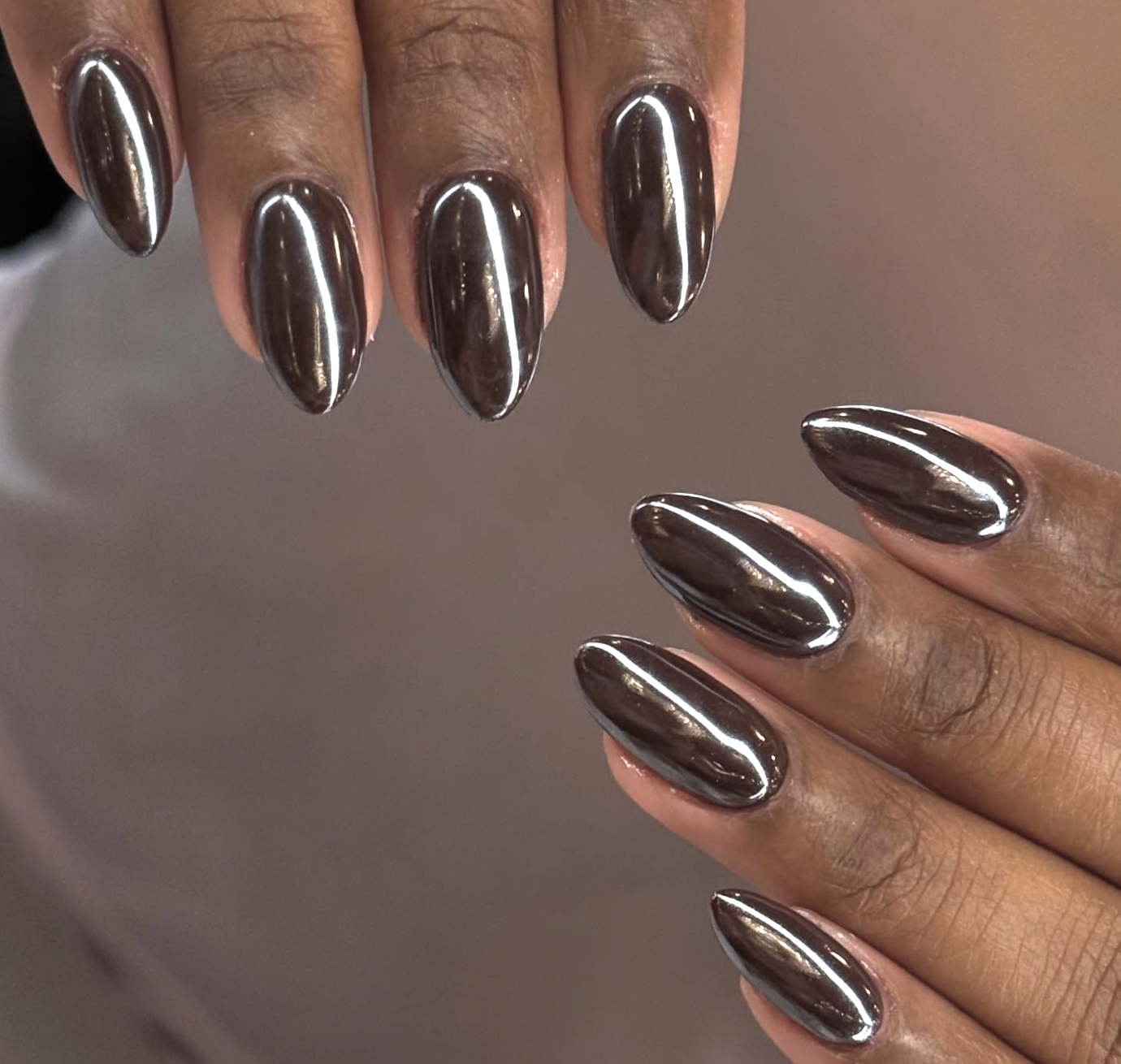 A close-up of glossy chocolate brown almond nails featuring a high-shine glazed pearl finish that catches the light.