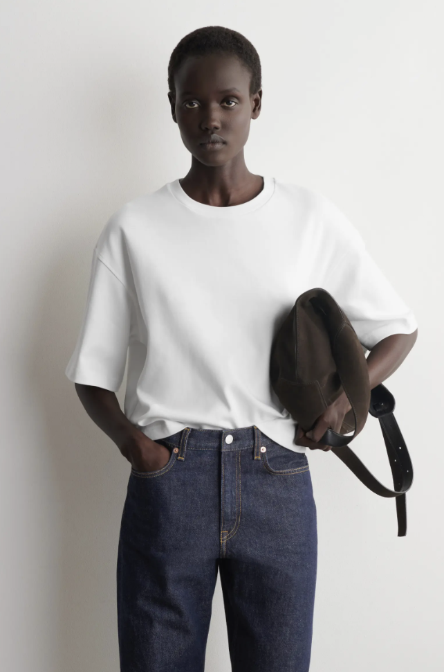 Close-up of a woman wearing an oversized white t-shirt tucked into dark wash jeans.