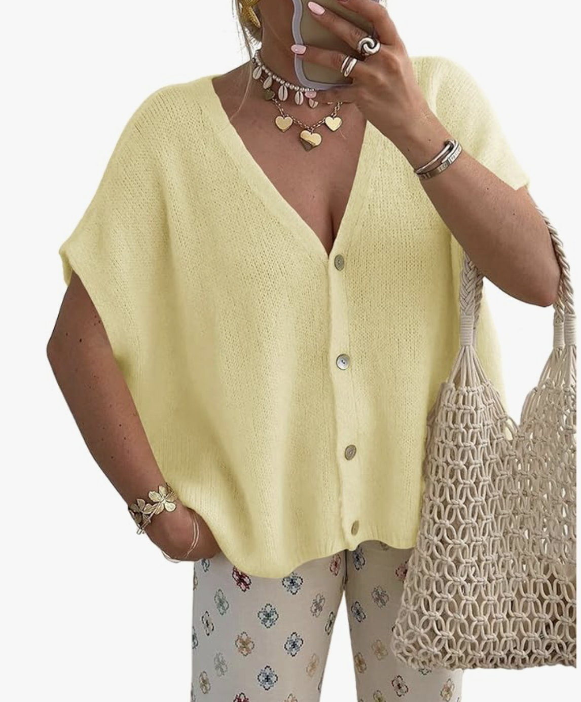 Close-up of a woman wearing a pale yellow, short-sleeve button-down knit cardigan sweater with tortoiseshell buttons, paired with white pants featuring a blue and brown geometric pattern.