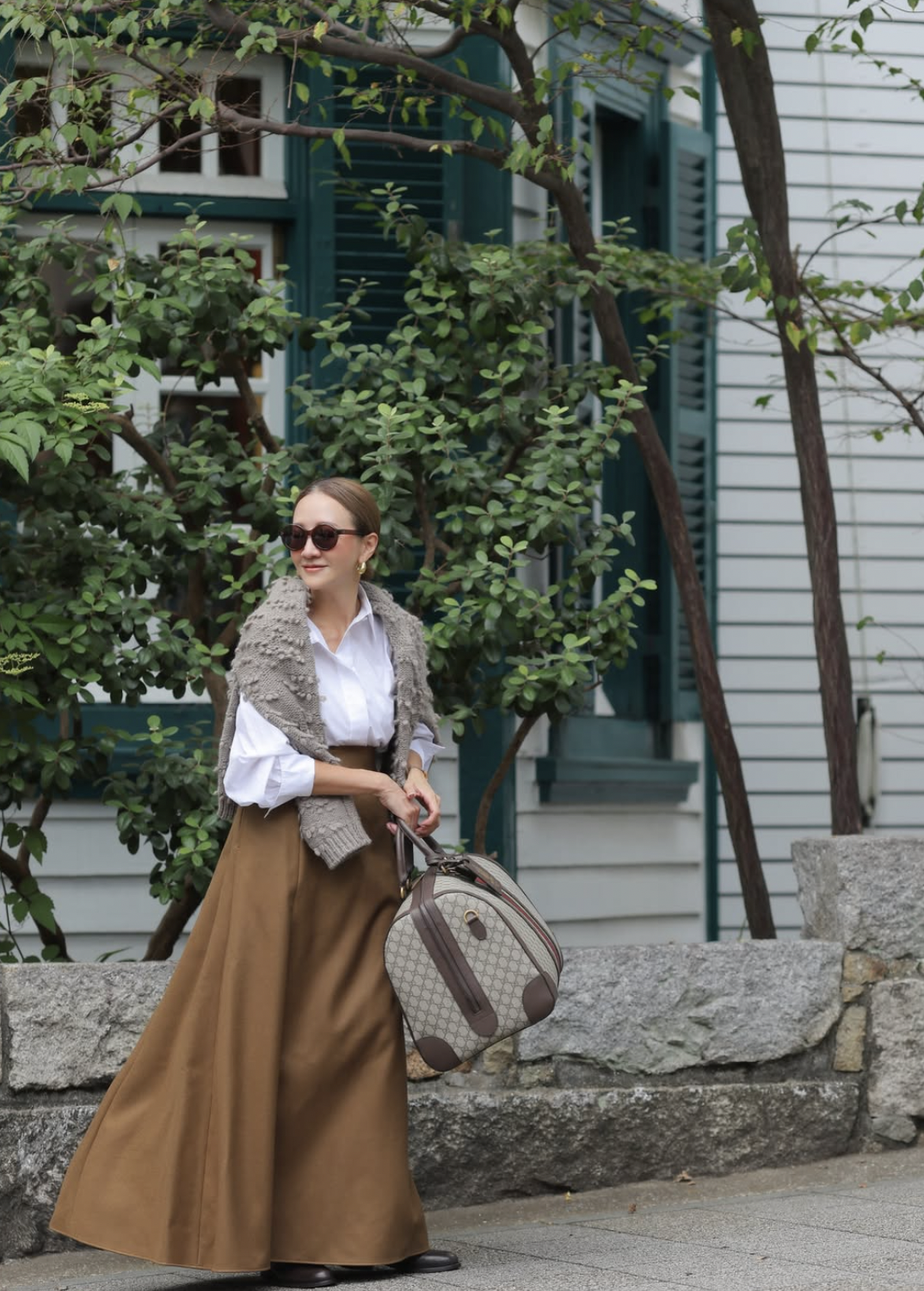 Woman wearing a camel A-line midi skirt with a white button-down, knit scarf and black loafers