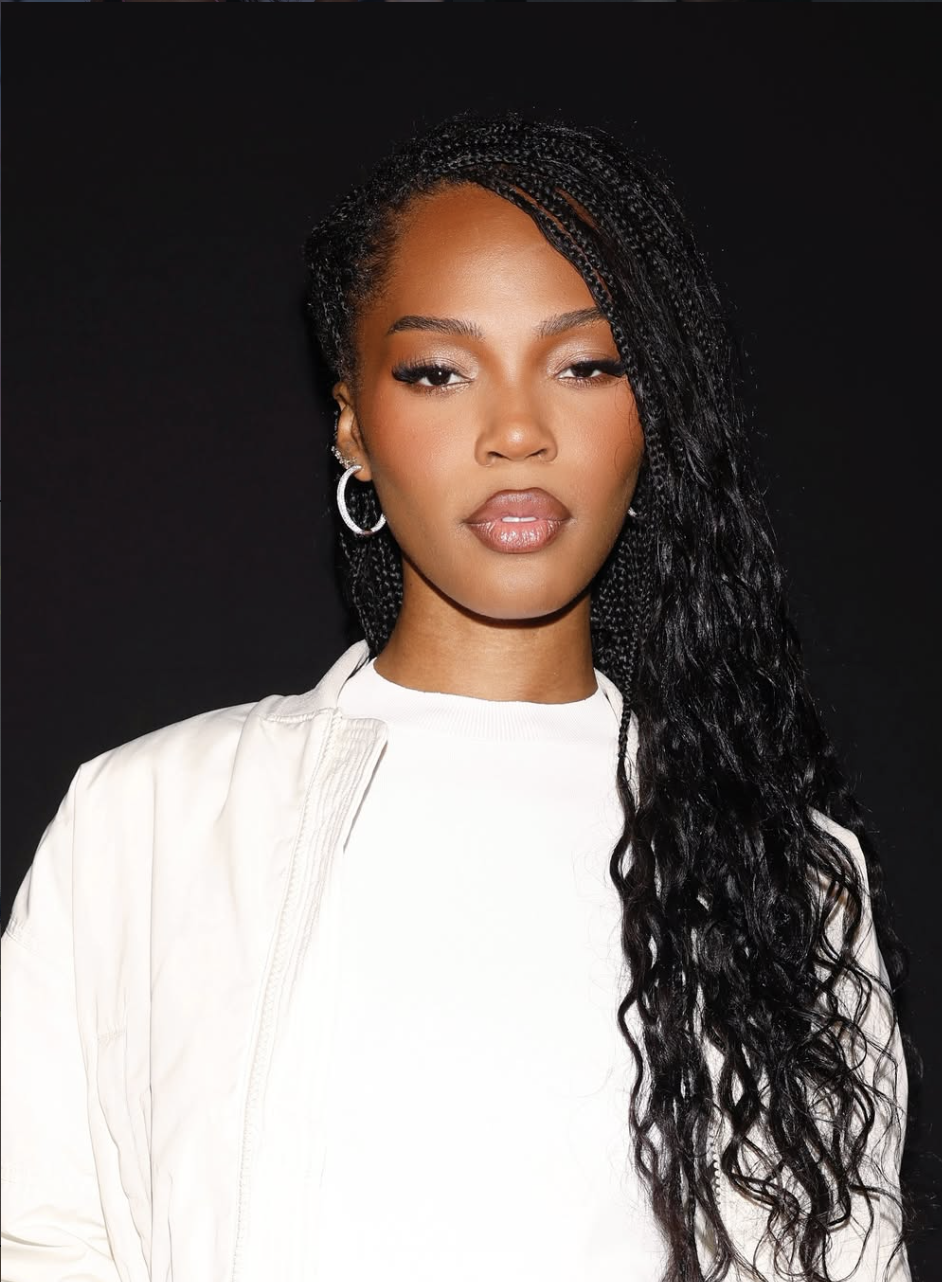 Content creator Quen Blackwell wearing long, neat protective micro braids and a high-neck white top, smiling gently while looking at the camera.