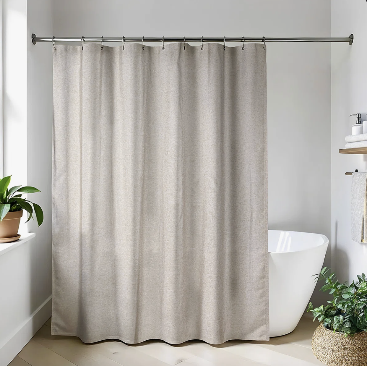 A light grey linen-look fabric shower curtain mounted on a silver rod, skimming the floor next to a potted green plant in a modern bathroom.