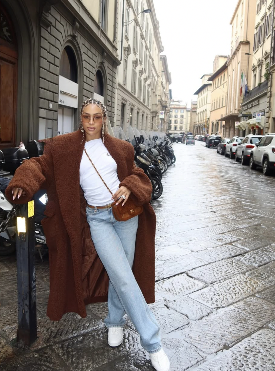 A fashion editor-inspired outfit featuring a simple white t-shirt tucked into high-waisted, light-wash straight-leg jeans, accessorized with a black leather belt and gold jewelry.