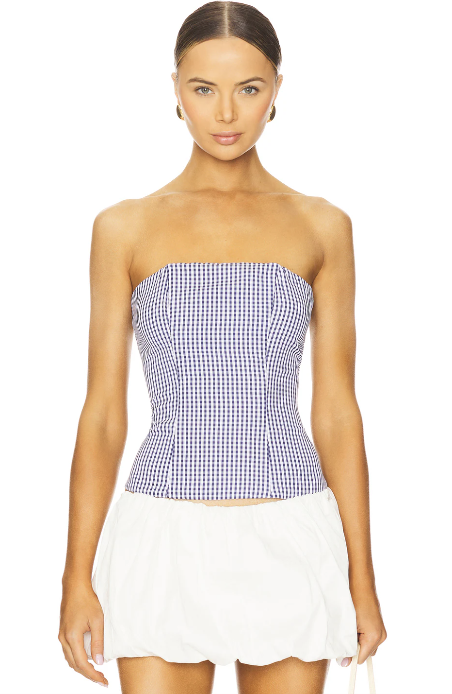 A woman wearing a fitted blue-and-white gingham print strapless corset-style top paired with white shorts, styled for a fresh, resort-casual vacation look.