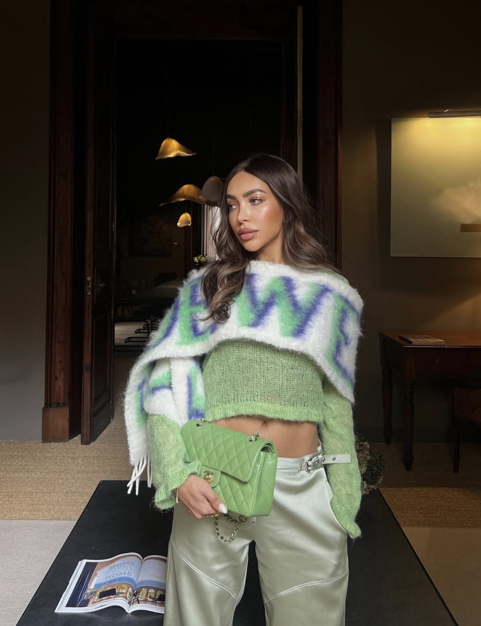 A woman wearing a monochromatic pistachio green outfit featuring a cropped fuzzy knit sweater, light green trousers, and a matching quilted designer handbag.
