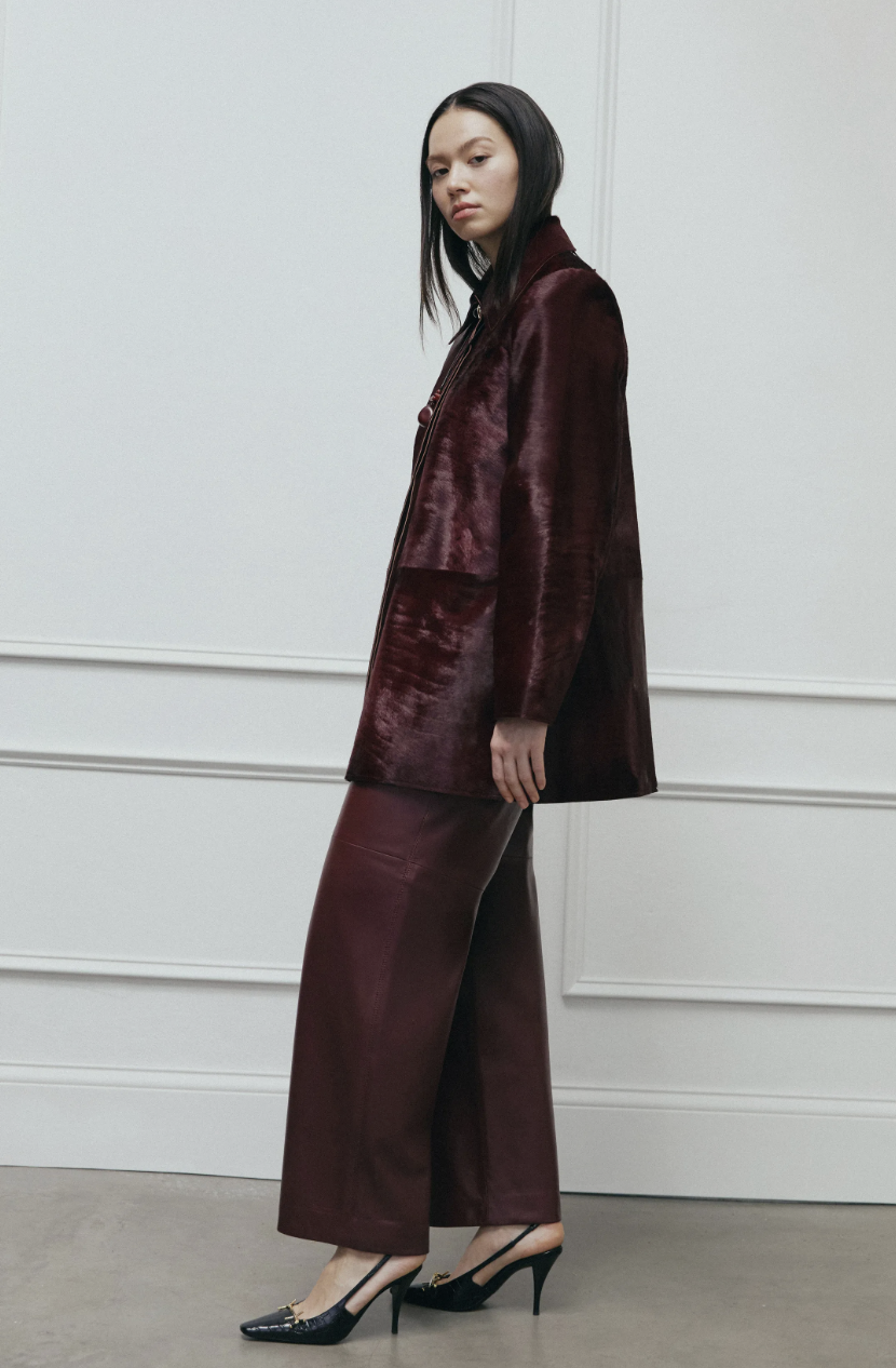 A model walks the Tanya Taylor Fall/Winter 2026 runway wearing a rich aubergine textured top and skirt, demonstrating the season's power neutral color trend.