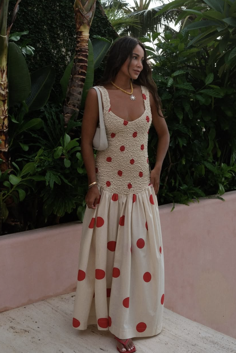 Petite woman wearing a white smocked maxi dress with large red polka dots, paired with minimalist red thong sandals.