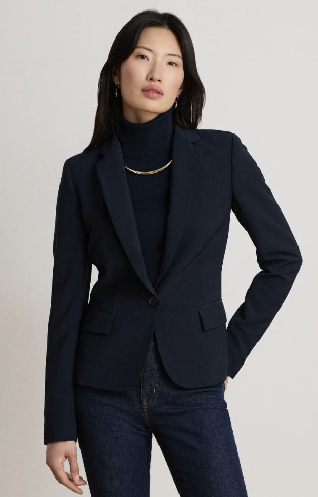 Woman wearing a classic navy tailored blazer styled with a dark turtleneck and dark-wash jeans.