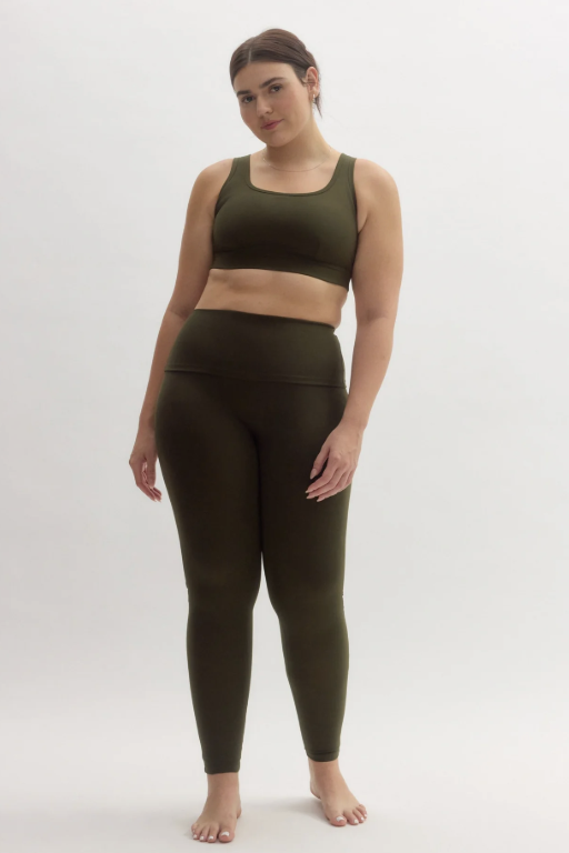 A plus-size model wearing the Girlfriend Collective Compressive High-Rise Legging and matching sports bra in olive green, featuring a supportive fit and functional side pockets for a structured everyday look.