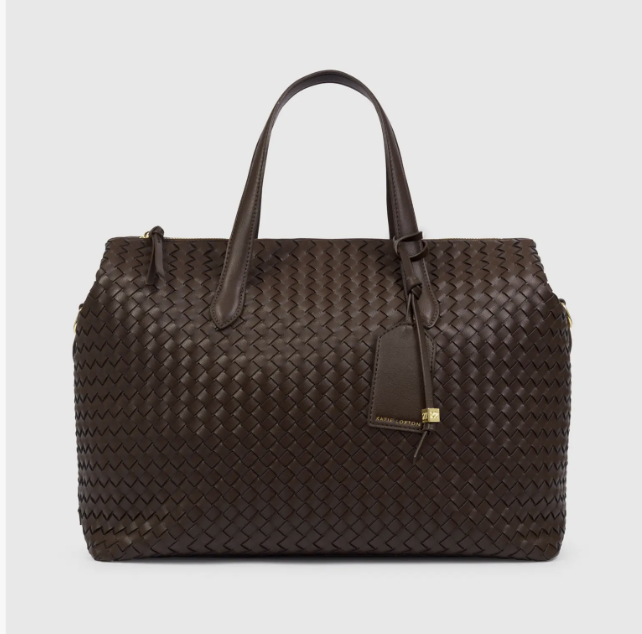 A chocolate brown woven leather tote bag with top handles, dual zipper closures, and a matching hanging luggage tag.