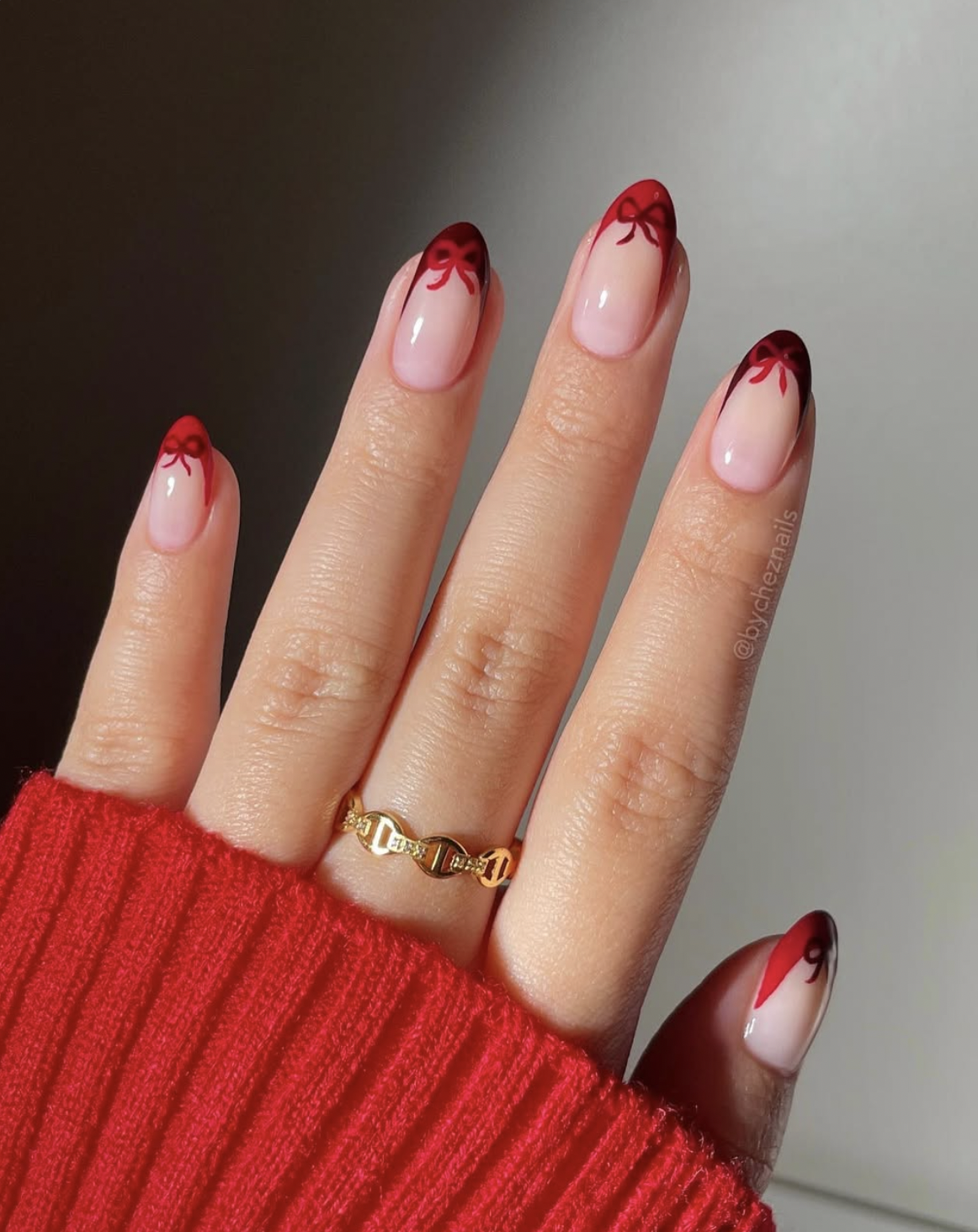 Sheer nude nails with red French tips and tiny Christmas bows