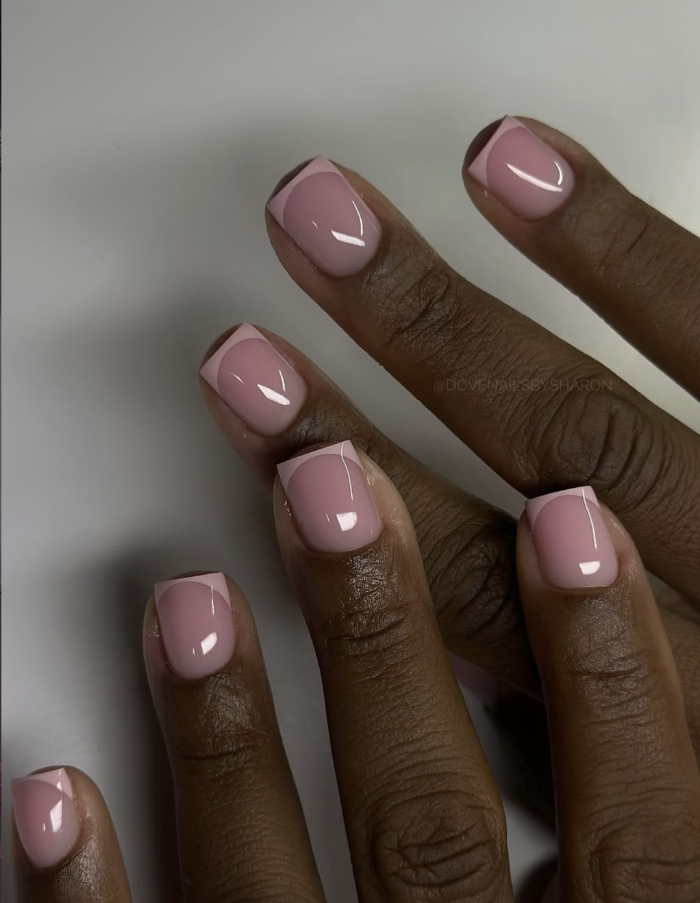 A close-up of short, square-shaped nails featuring a sheer mauve-pink base with a crisp, classic light pink French manicure tip.