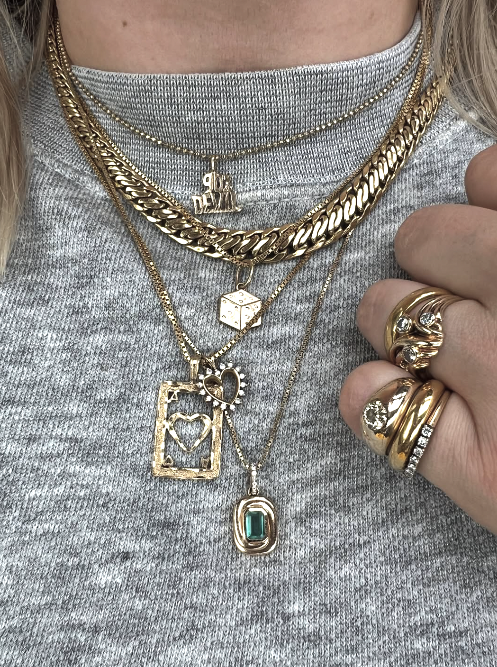 Layered gold pendant necklaces with an emerald charm on a grey sweater.