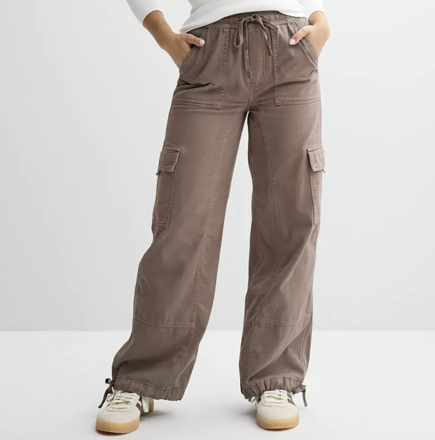 A person wearing high-waisted, wide-leg khaki cargo pants with large side pockets, styled with white and tan leather sneakers.