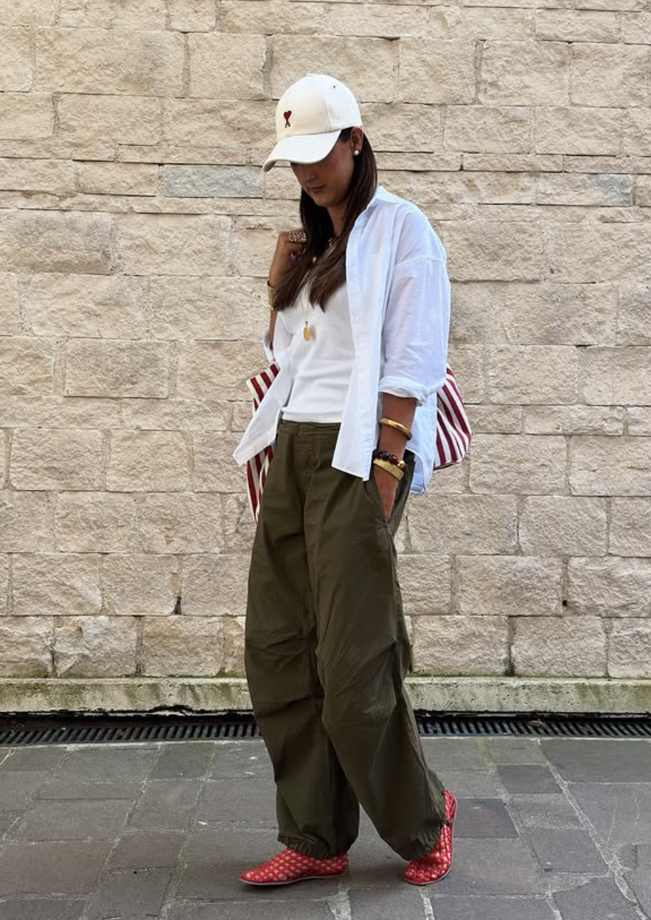 A person wearing an oversized white long-sleeve button-down shirt over a white tee, paired with wide-leg olive green cargo pants and red patterned flats.