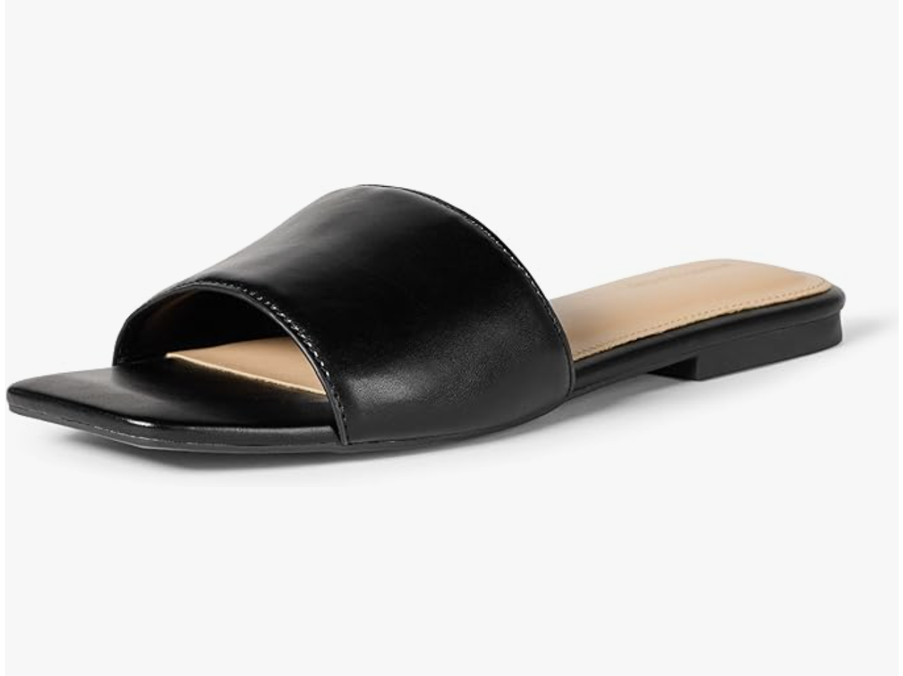 A pair of black leather flat slide sandals with a single wide strap, a minimal and chic footwear choice for styling white wide-leg jeans.