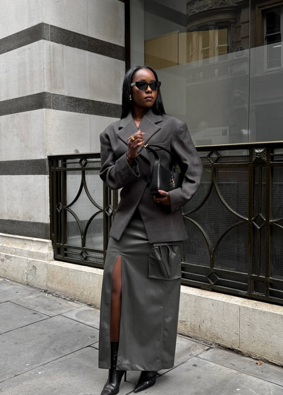 A woman wearing a white graphic t-shirt tucked into dark straight-leg trousers, styled with an oversized plaid blazer and loafers for a comfortable workwear look.