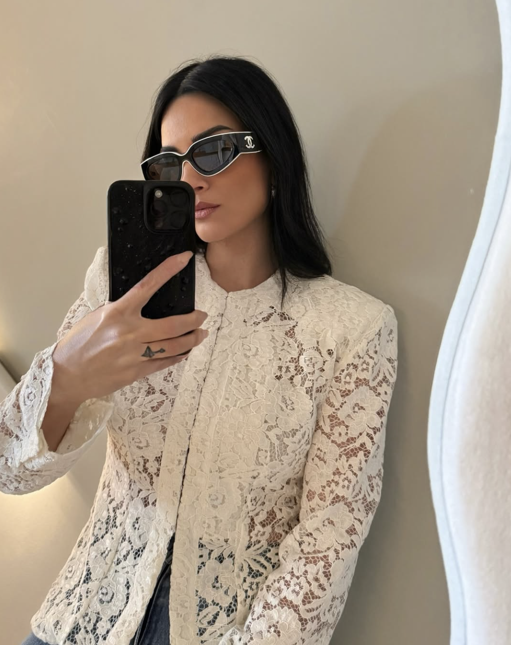 A woman taking a mirror selfie wearing a beige long-sleeve lace button-up blouse with a structured collar, styled with black sunglasses and a sleek hairstyle.
