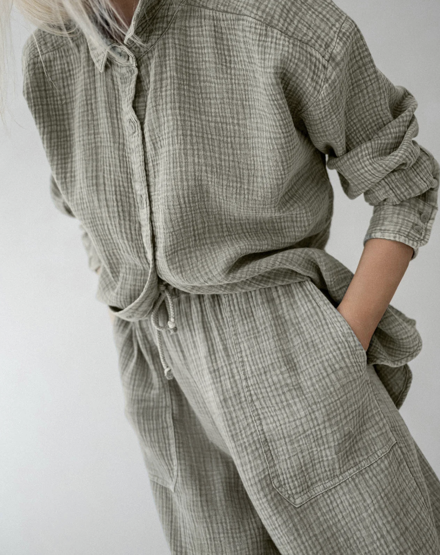 A person wearing an oversized sage green linen button-down shirt and matching wide-leg trousers with grey pointed-toe kitten heels.