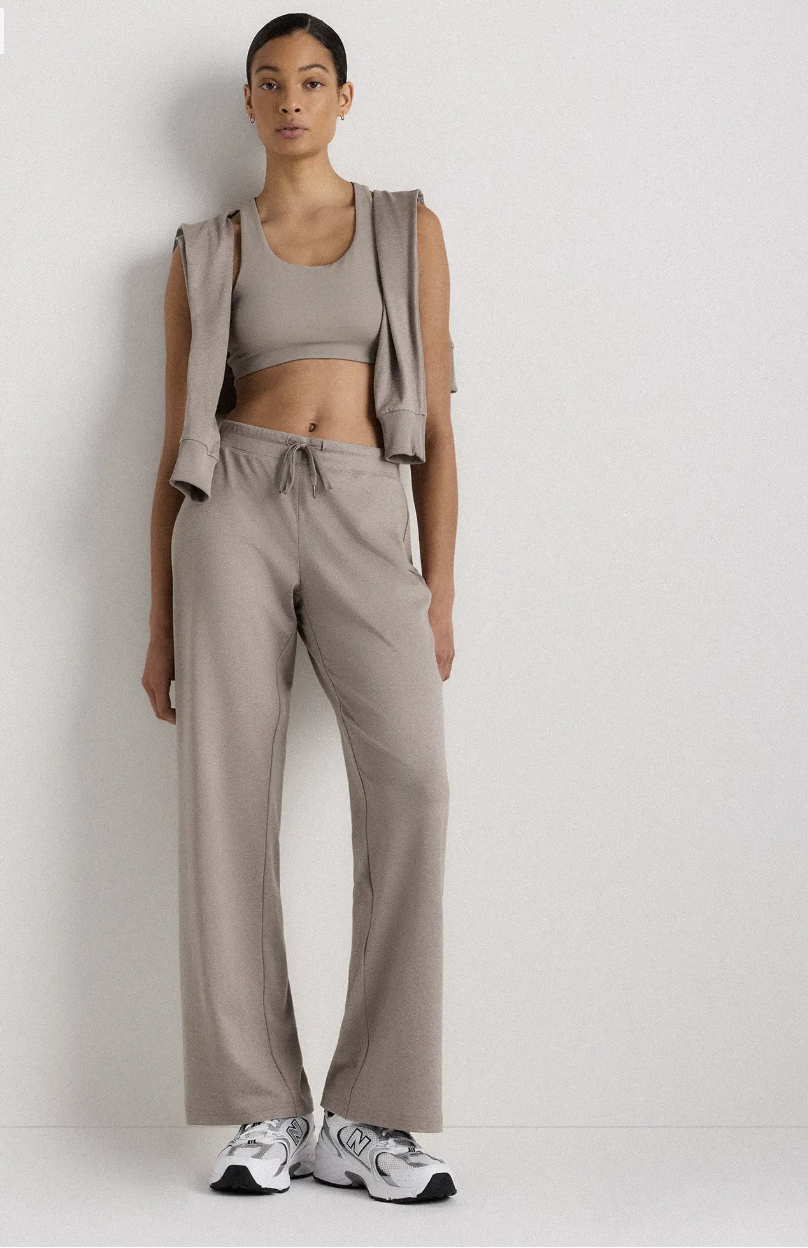 Professional traveler's pick: the Quince Flowknit Wide Leg Pants in a neutral taupe, styled as a monochromatic set with a matching sports bra and draped sweatshirt for a comfortable spring break travel look.