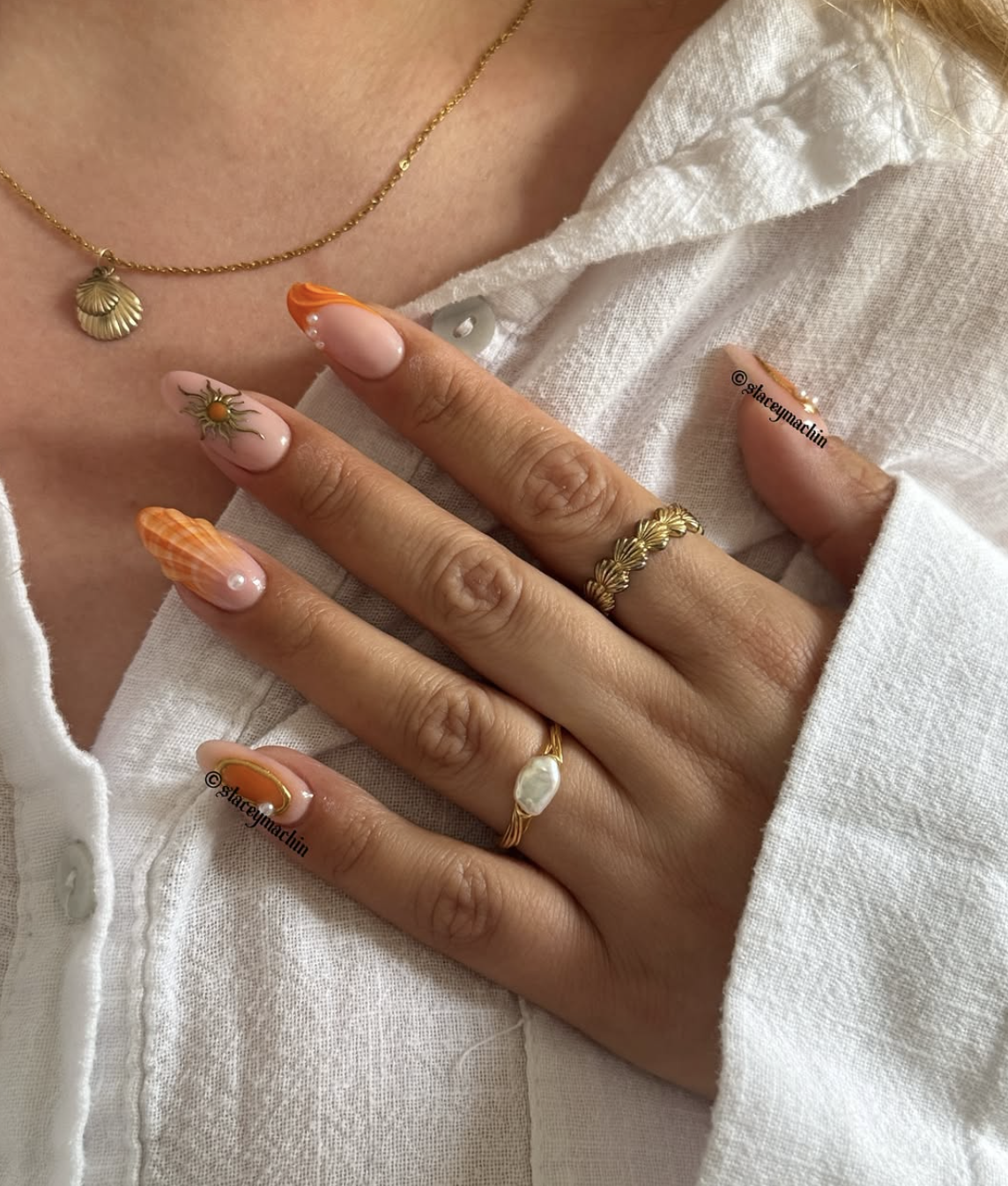 Long almond-shaped gel nails in a vibrant coral-orange with 3D seashell textures and pearl accents.