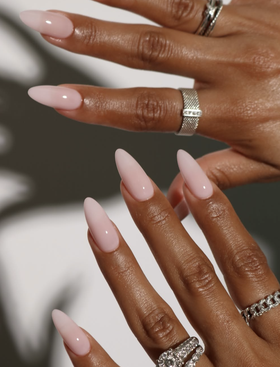 Long, almond-shaped nails with a glossy, semi-sheer blush pink base coat topped with a soft, luminous pearl chrome glaze.