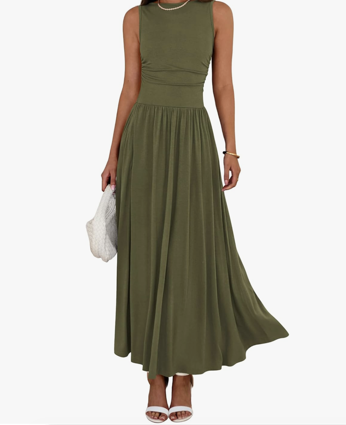 Front view of a woman wearing a sleeveless, olive green pleated A-line midi dress with a high neckline, holding a white woven handbag and wearing white ankle-strap sandals.