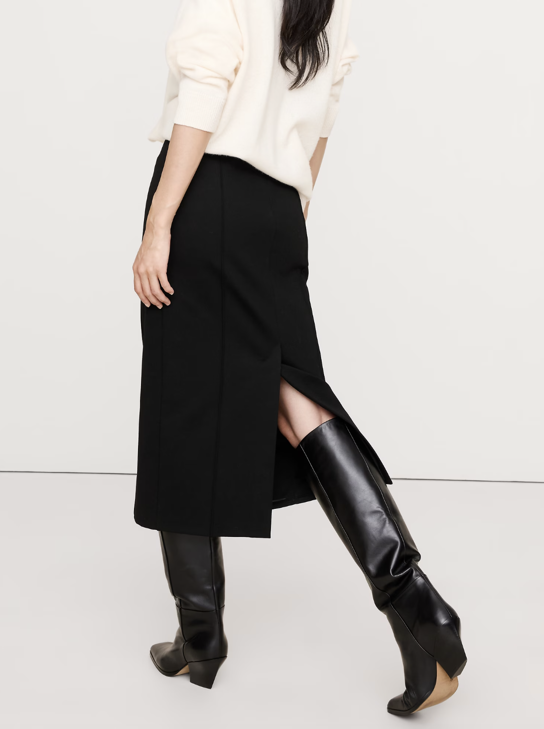 A professional work outfit featuring a black midi pencil skirt with a front slit and a white sweater, ideal for styling as a business casual look with sneakers.