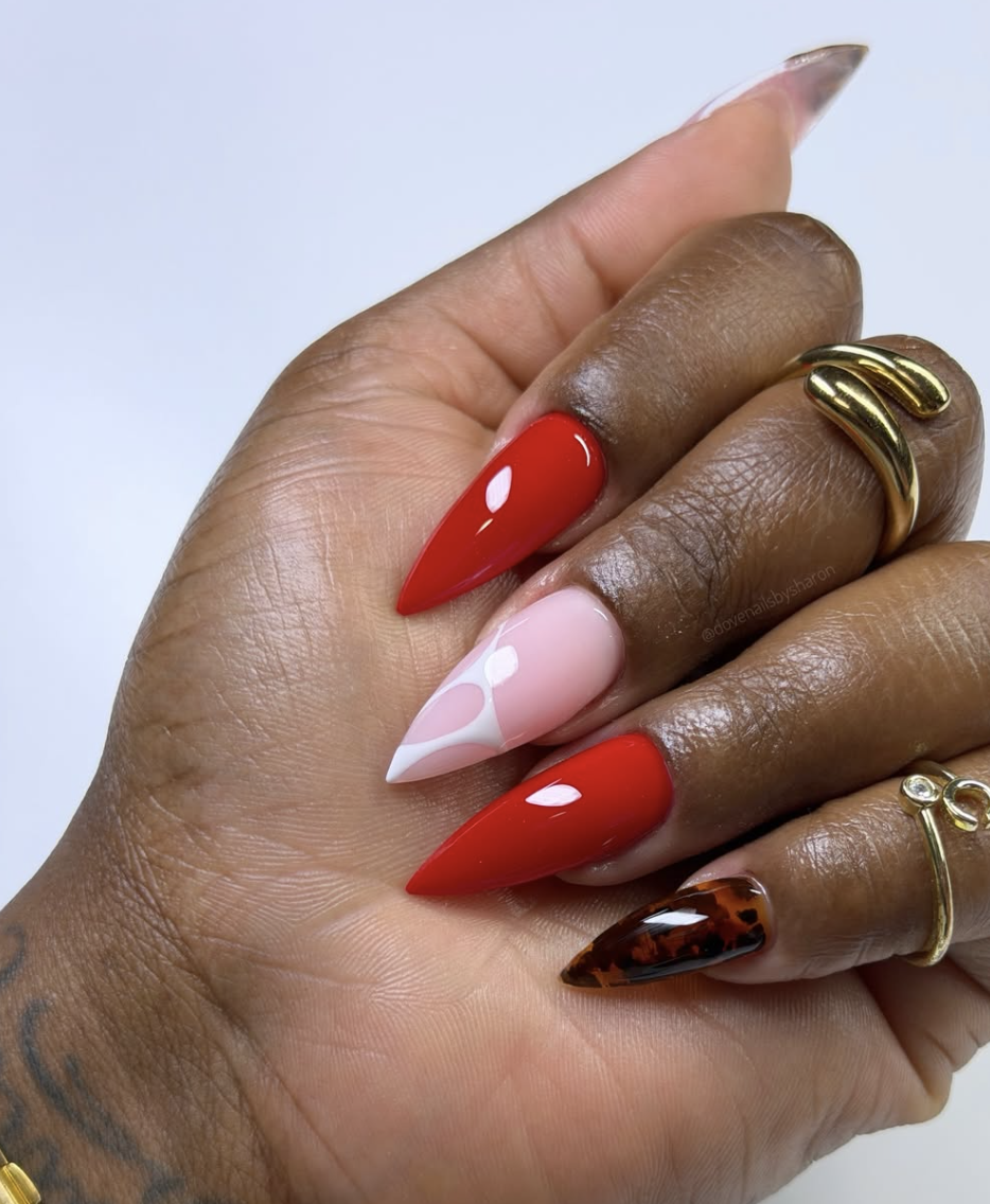 Close-up of a hand with long, sharp stiletto-shaped nails featuring a high-coverage, ultra-glossy cherry red manicure, accented with multi-toned pink and white side tips.