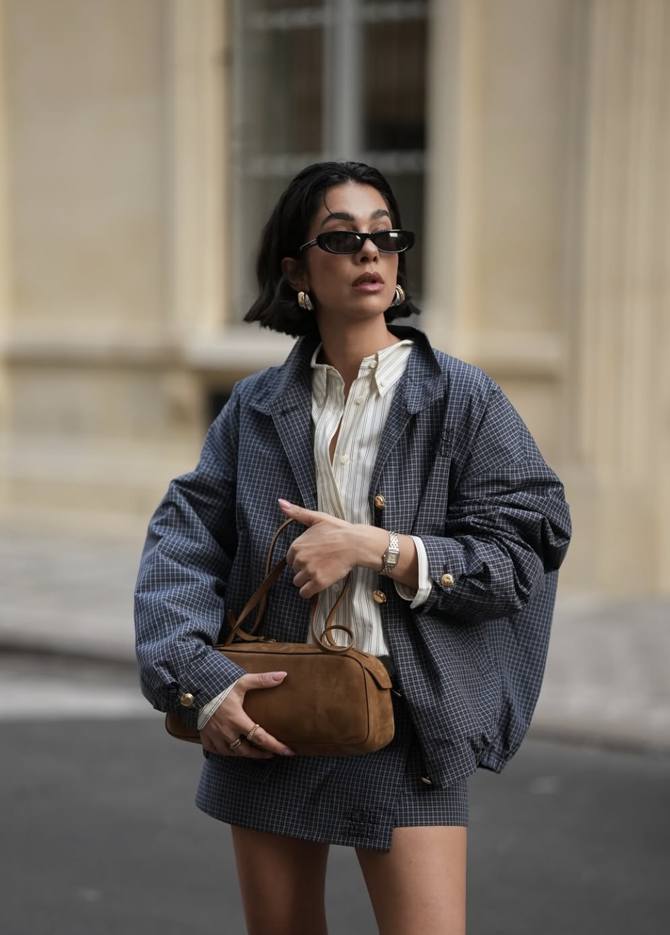 A woman balancing a long torso and short legs by wearing a high-waisted plaid mini skirt with an oversized blazer and a tucked-in button-down shirt.