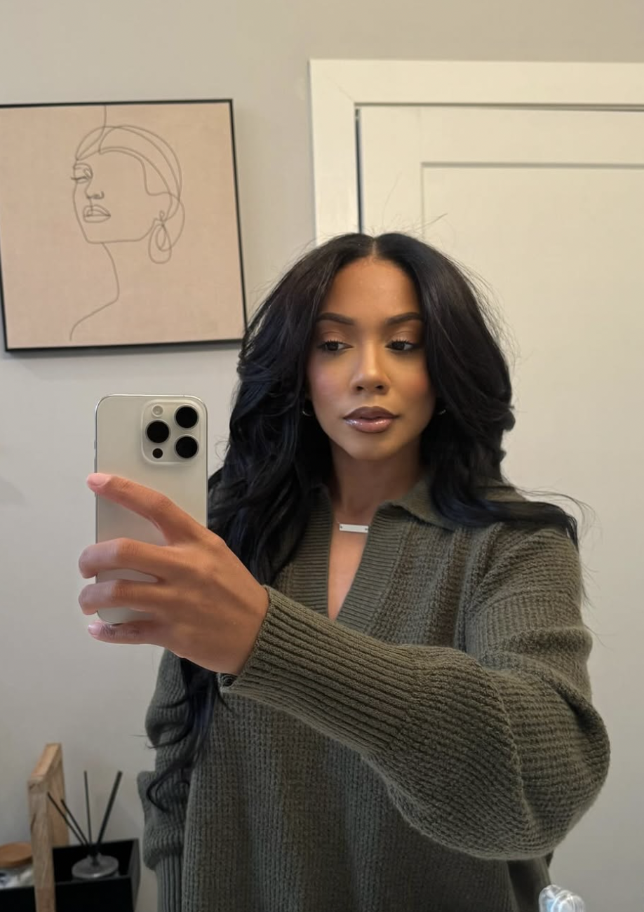 A woman with an oval face shape wearing long, dark waves with soft curtain bangs that frame the forehead and cheekbones.