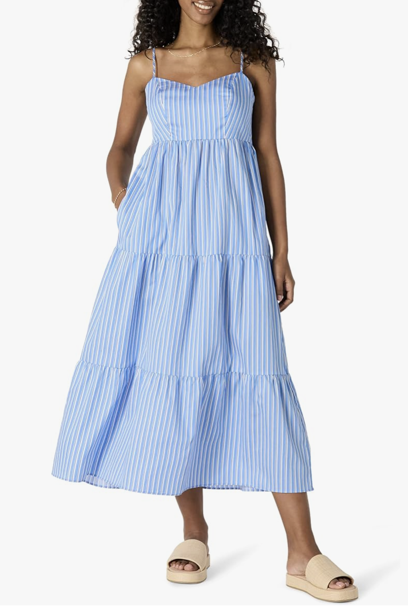 A woman wearing a blue and white vertical striped tiered fit-and-flare midi dress with spaghetti straps and a smocked back.