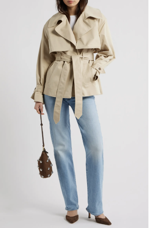A woman wearing light-wash straight-leg jeans paired with an exaggerated crop trench coat in tan, styled with brown pointed-toe heels and a studded brown leather handbag.