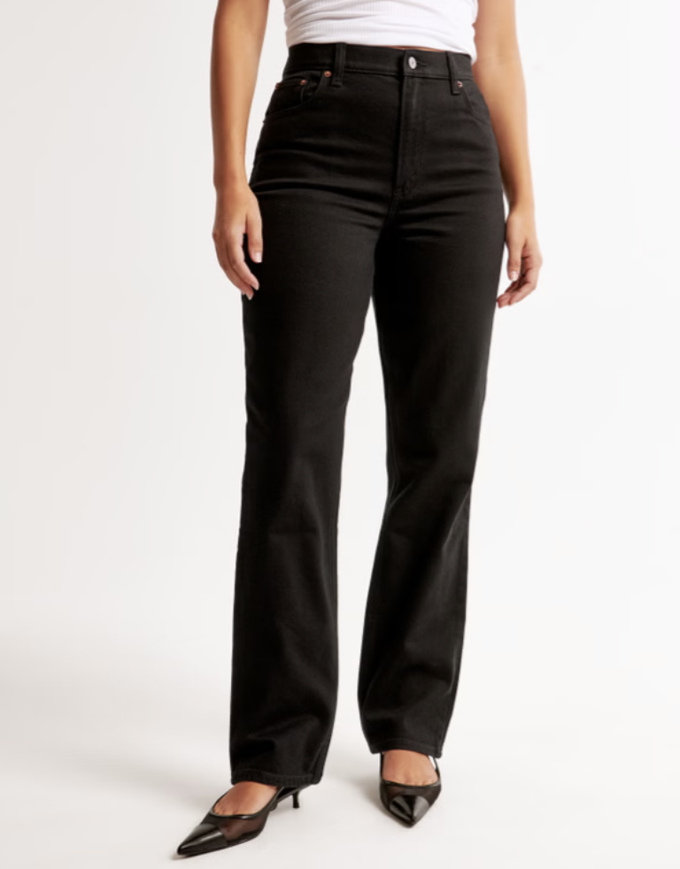 A woman wearing black Abercrombie Curve Love Ultra High Rise 90s Straight Jeans paired with black pointed-toe heels. These jeans feature an extra 2 inches through the hip and thigh to eliminate waist gap and provide a flattering curvy fit.
